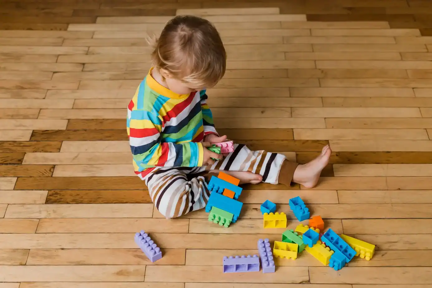 Niño de 1 a 2 años jugando en el suelo con bloques de construcción de colores, explorando y manipulando objetos propios de su edad.