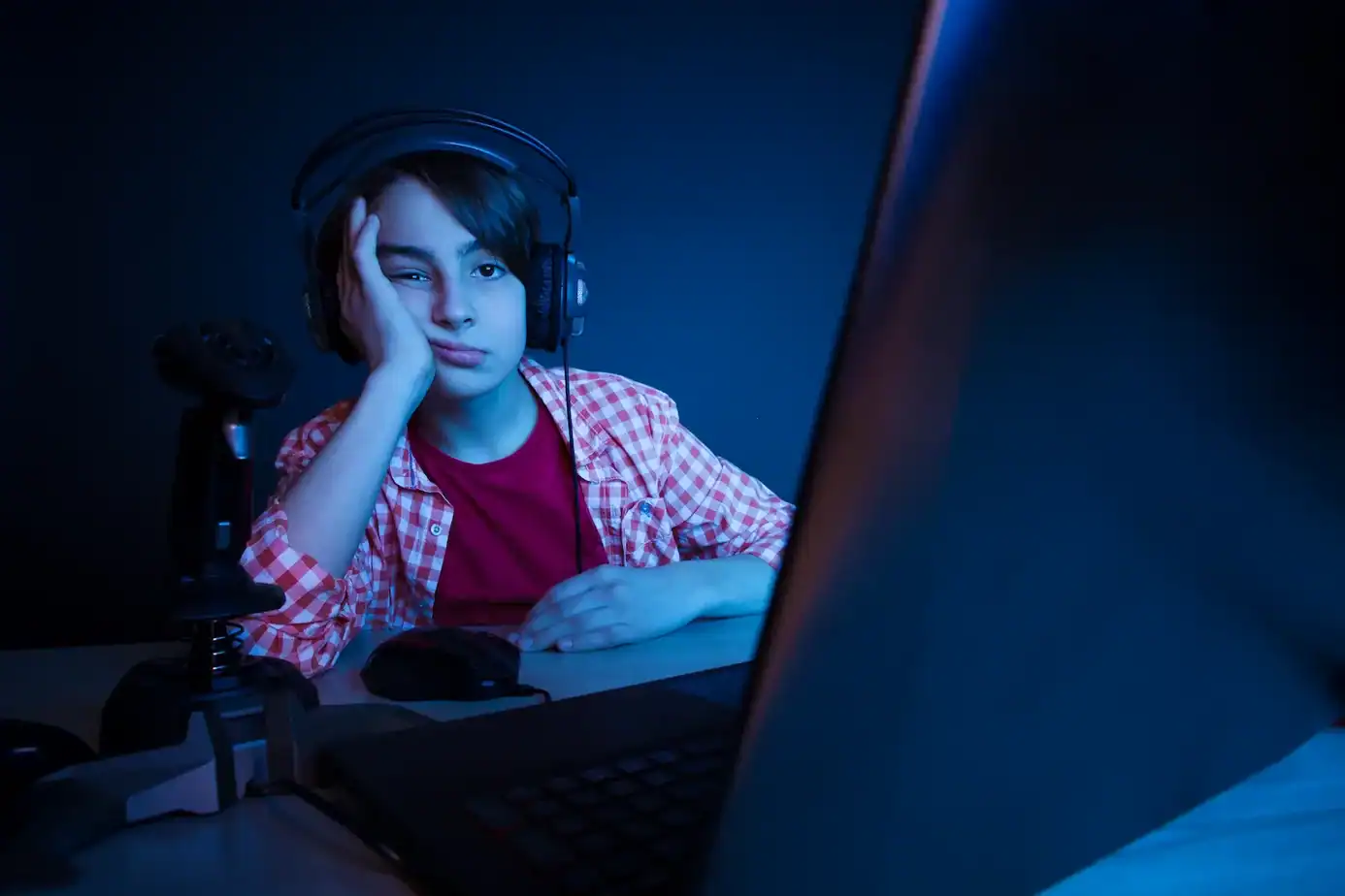 Adolescentes y pantallas: adolescente frente a la pantalla del ordenador usando auriculares en una habitación oscura