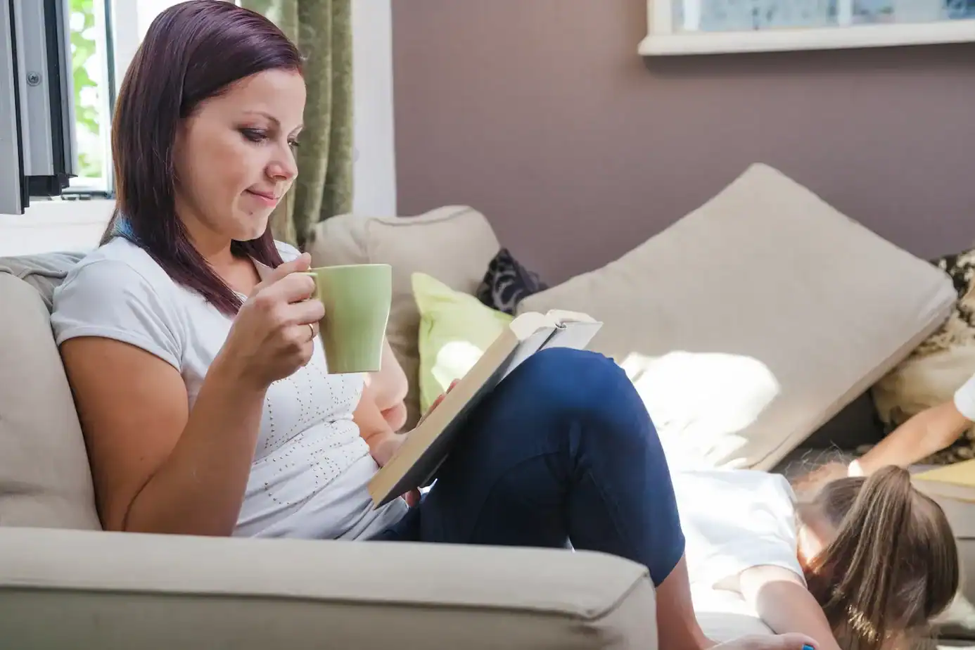 salir del mom mode es preservar espacios personales madre sentada en el sofá leyendo y tomando café mientras su hijo juega representando la importancia del espacio personal en la maternidad
