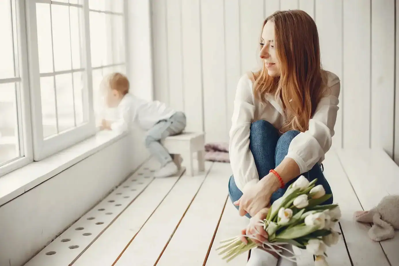 salir del mom mode madre sentada mirando por la ventana mientras su hijo juega representando la necesidad de espacio personal en la maternidad