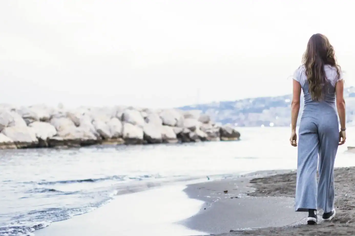 Mujer caminando sola junto al mar durante un momento de reflexión y autocuidado tras una etapa de agotamiento emocional.