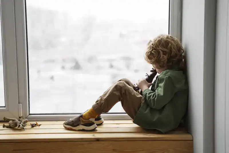 niño sentado solo en el alféizar de una ventana mirando hacia fuera consecuencia de la pasivo-agresividad en pareja
