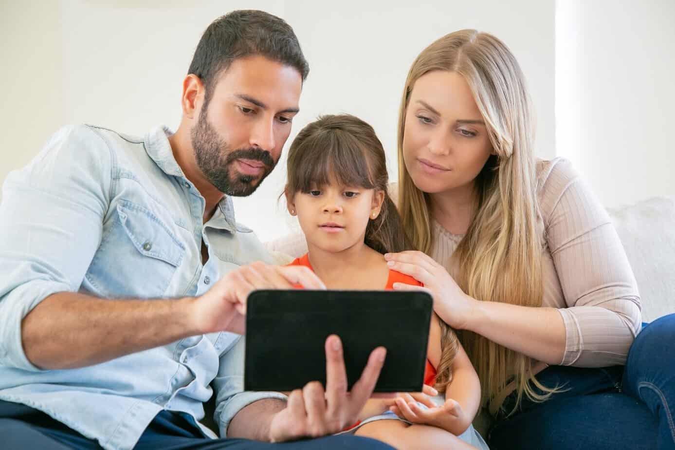 niños y pantallas: Padres acompañando a su hija mientras utiliza una tableta en casa