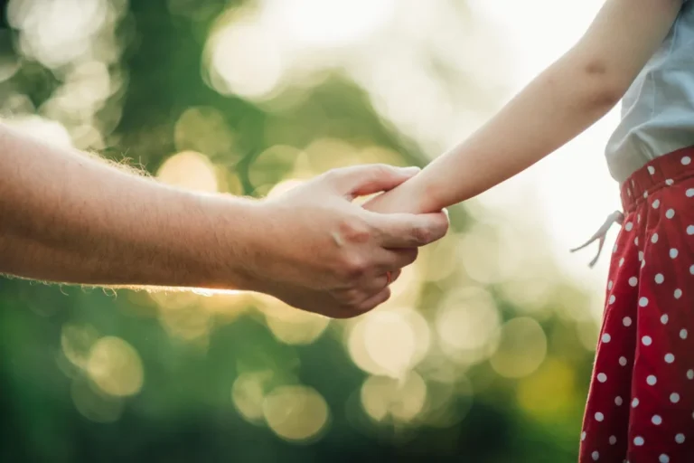 Un adulto sostiene la mano de una niña al aire libre