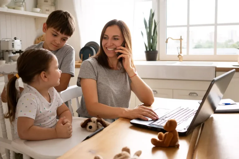 Inicio 4 Madre teletrabajando desde casa junto a sus dos hijos, conciliando trabajo y vida familiar.